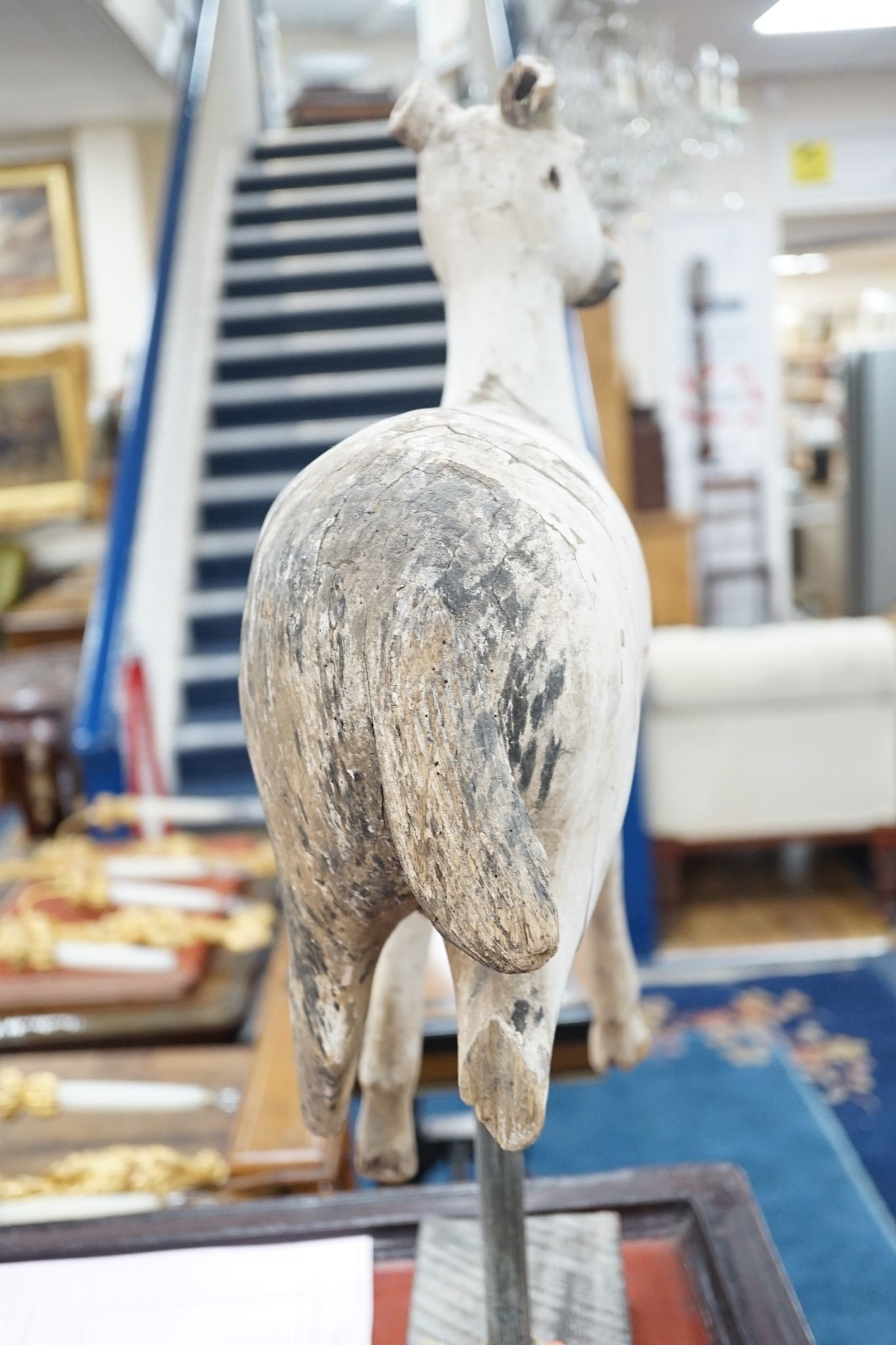 A carved and painted wood model of a goat, with distressed paint, on stand. 66cm